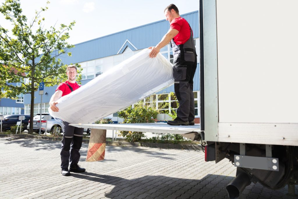two men in red shirts and black pants on moving truck getting a mattress out