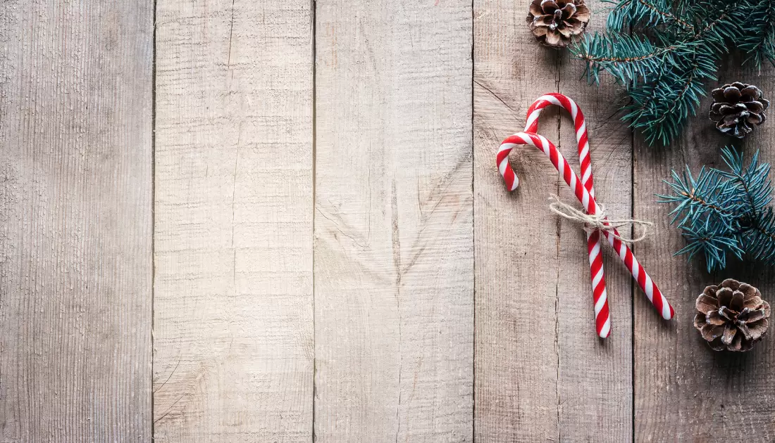 Two candy canes tied together with a string lying next to pine cones and green fir branches on a rustic wooden surface, creating a cozy holiday atmosphere.